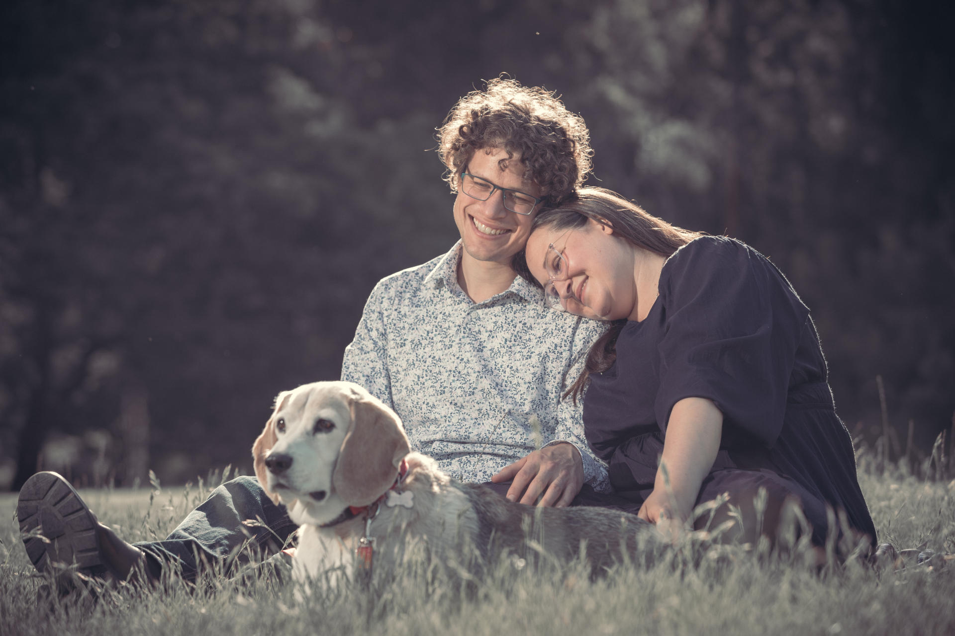 Libby & Tim sitting in the grass with Charlie the beagle.